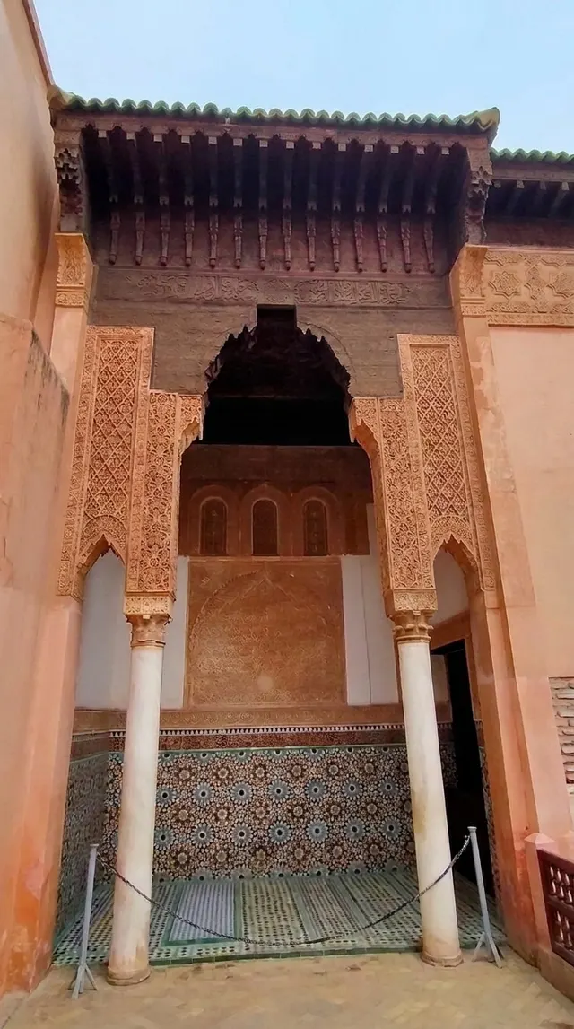 A carved stucco portico on marble columns above a zellige dado, seen from the courtyard