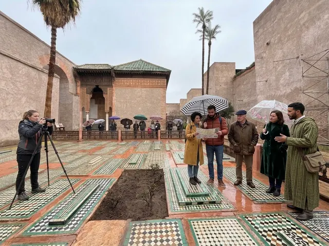 A guide in a djellaba explaining the site to visitors in the garden of tombs on a wet day