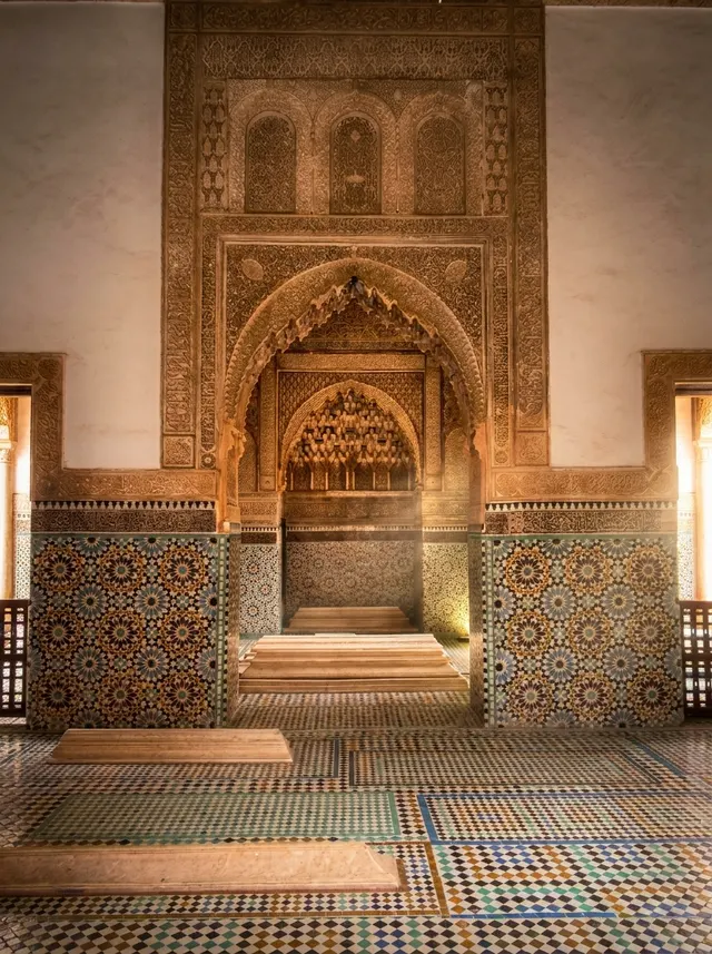 The carved mihrab wall and zellige panels of the prayer hall, with marble grave slabs on the floor